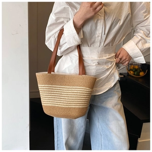 Detail of hand-woven straw tote with horizontal beige stripes and brown leather strap