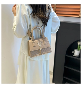 Detail of beige shoulder bag featuring quilted texture and elegant gold V-logo with tassel