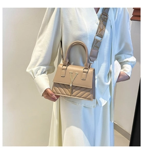 Close-up of beige PU leather handbag with gold V hardware, tassels and wide strap
