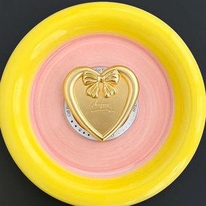 Detail of a golden heart phone stand with 3D bow and happy text on a pink ceramic tray