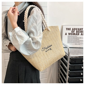 Close-up of woven straw tote bag featuring Fashion xing embroidery and white rope handles