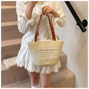Detail of hollow-out beige straw woven tote with brown leather strap handle on stairs