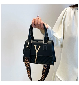 Close-up of black quilted handbag with gold V logo, tassel and patterned strap
