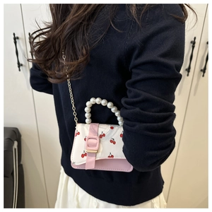 Close-up of pink cherry print mini crossbody bag with pearl handle and gold chain
