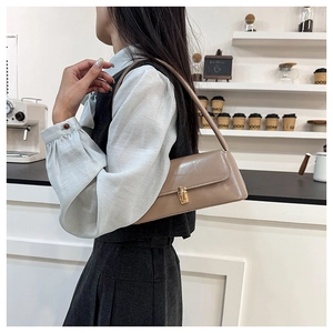 Side view of a khaki leather baguette bag with gold twist lock worn as an underarm bag