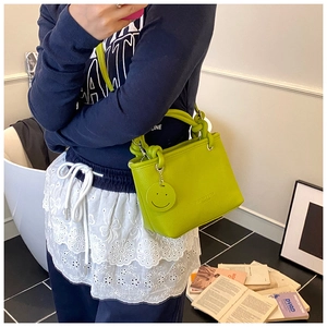 Detail view of grass green litchi grain PU handbag with a smiley pendant for women