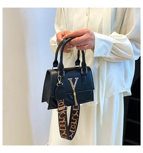 Close-up of black crossbody bag with golden V-logo and wide patterned fabric strap