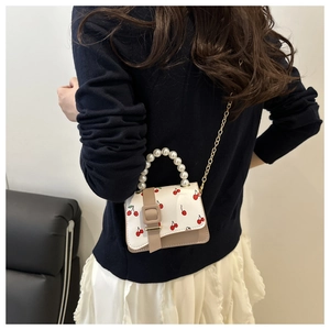 Detail of mini square bag with cherry print, pearl handle and gold chain strap