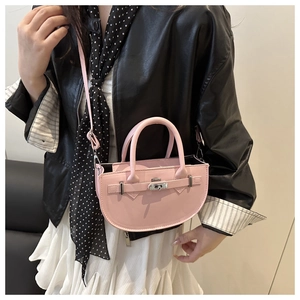Détail d'un sac selle en cuir rose avec fermoir en métal doré porté sur une veste