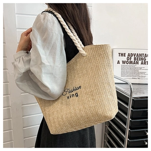 Detail of straw tote bag featuring white rope handles and black cursive lettering