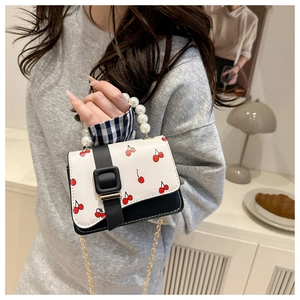 Detail of mini cherry print bag with pearl handle and golden chain strap in home setting