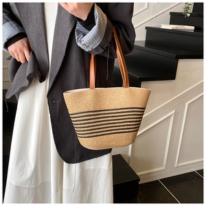 Detail of hand-woven straw tote with black stripes and brown leather handle