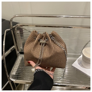 Détail d'un sac seau tissé avec chaîne argentée, cordon et ornement en perle