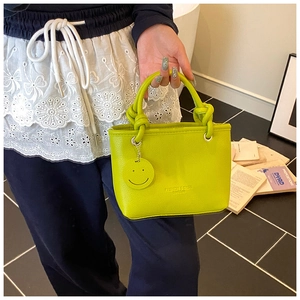 Close-up of neon green leather bucket bag with top handles and smiley face charm details