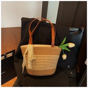Detail of straw tote bag with beige lace bow and brown leather strap on a chair