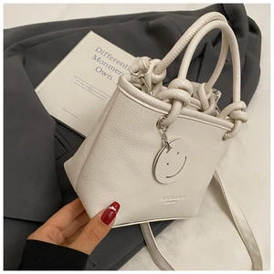 Detail of off-white lychee texture leather bucket bag with knot handle and smiley charm