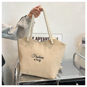 Detail of beige canvas tote bag featuring black embroidery and thick cotton rope handles