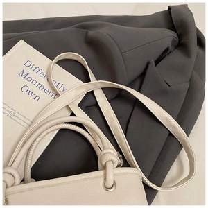 Detailed close-up of cream lychee grain leather bucket bag on dark grey textured fabric