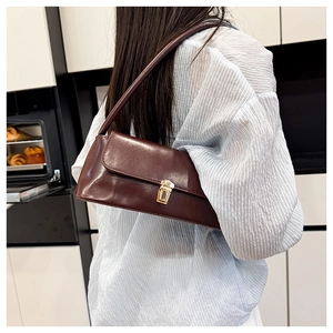 Close-up of retro brown baguette underarm bag with gold lock worn by a model