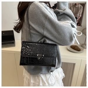 Detail of a chic black crocodile embossed shoulder bag with gold chain and metal buckle