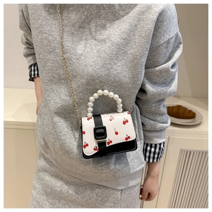 Detail of white mini crossbody bag with cherry print, pearl handle and gold chain strap