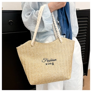 Detail of woven straw tote bag featuring black embroidery and thick cotton rope handles