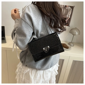 Detail of glossy black crocodile pattern shoulder bag with metallic chain and buckle