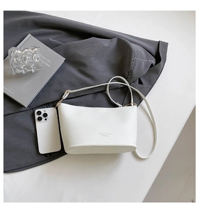 Détail du sac seau blanc en cuir grainé avec logo embossé sur un tissu gris élégant