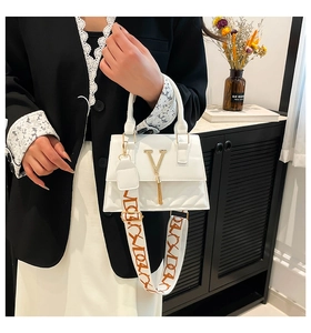 Detail view of white quilted faux leather handbag with golden V logo and tassel charm