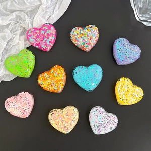 Set of 10 colorful sequin heart phone socket grips on a sleek black surface background