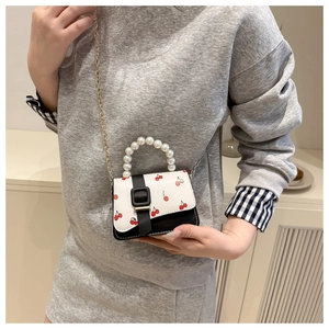Detail of a chic cherry print handbag featuring pearl handles and a gold chain strap