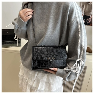 Detail of black crocodile pattern crossbody bag with silver buckle worn by a model