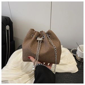 Détail d'un sac seau tressé marron avec chaîne argentée et cordons à perles décoratives