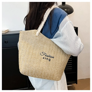 Close-up of beige woven straw tote bag with black embroidered text and thick rope handles