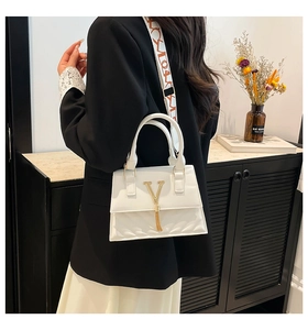 Detail of white leather bag with gold V-buckle, fringe tassel and printed wide strap