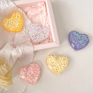 Five colorful sequin heart phone grips in pink, yellow, and purple on gift box