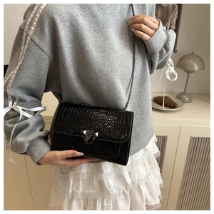 Detail of black crocodile texture shoulder bag with triangular buckle worn by a model