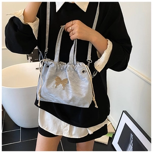 Detail of light blue pleated drawstring bucket bag with gold butterfly accent and pearl strap
