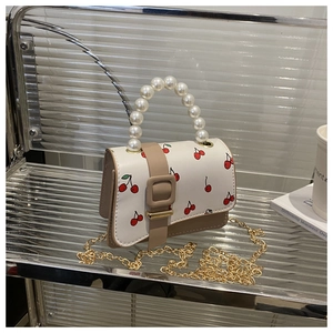 Detail of cherry print handbag featuring pearl handle and golden chain strap