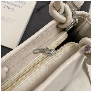 Detail view of cream lychee texture leather bag with silver zipper and knot handle