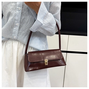Detail of dark brown leather shoulder bag with gold square buckle worn by a model