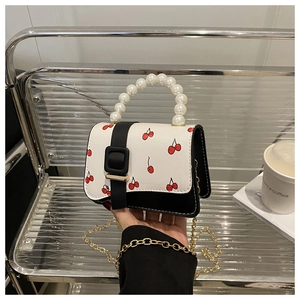 Close-up of cherry print mini bag with pearl handle and golden chain strap detail