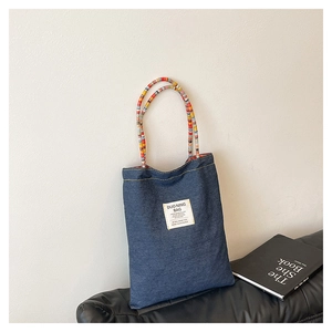 Détail du sac bandoulière en denim bleu avec anses tissées colorées et étiquette blanche