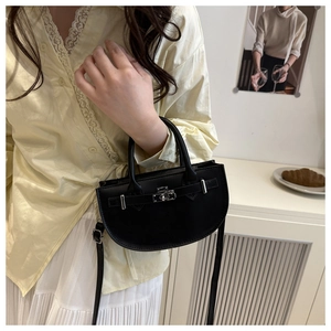 Gros plan du sac demi-lune en cuir noir avec boucle argentée porté par un modèle