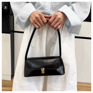 Close-up of a black leather baguette bag with a gold metal clasp held by a model