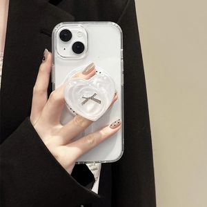 Sleek heart phone grip with bow detail on a clear iPhone case held by a model