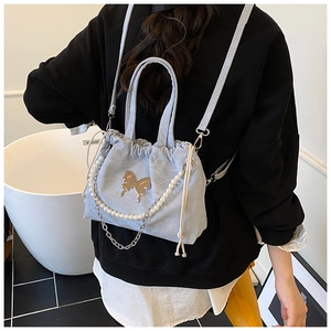 Light blue bucket bag with golden butterfly charm and pearl chain shown on model