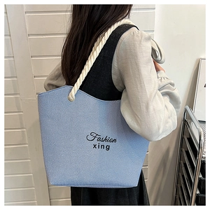 Macro detail of a light blue canvas tote bag with thick white rope handles and black lettering