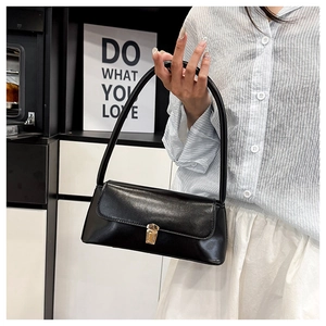 Detail of black faux leather baguette bag with golden metal buckle and slim shoulder strap