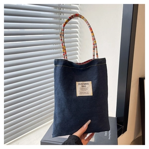 Détail d'un sac cabas en denim bleu avec anses en corde tressée et étiquette tissée